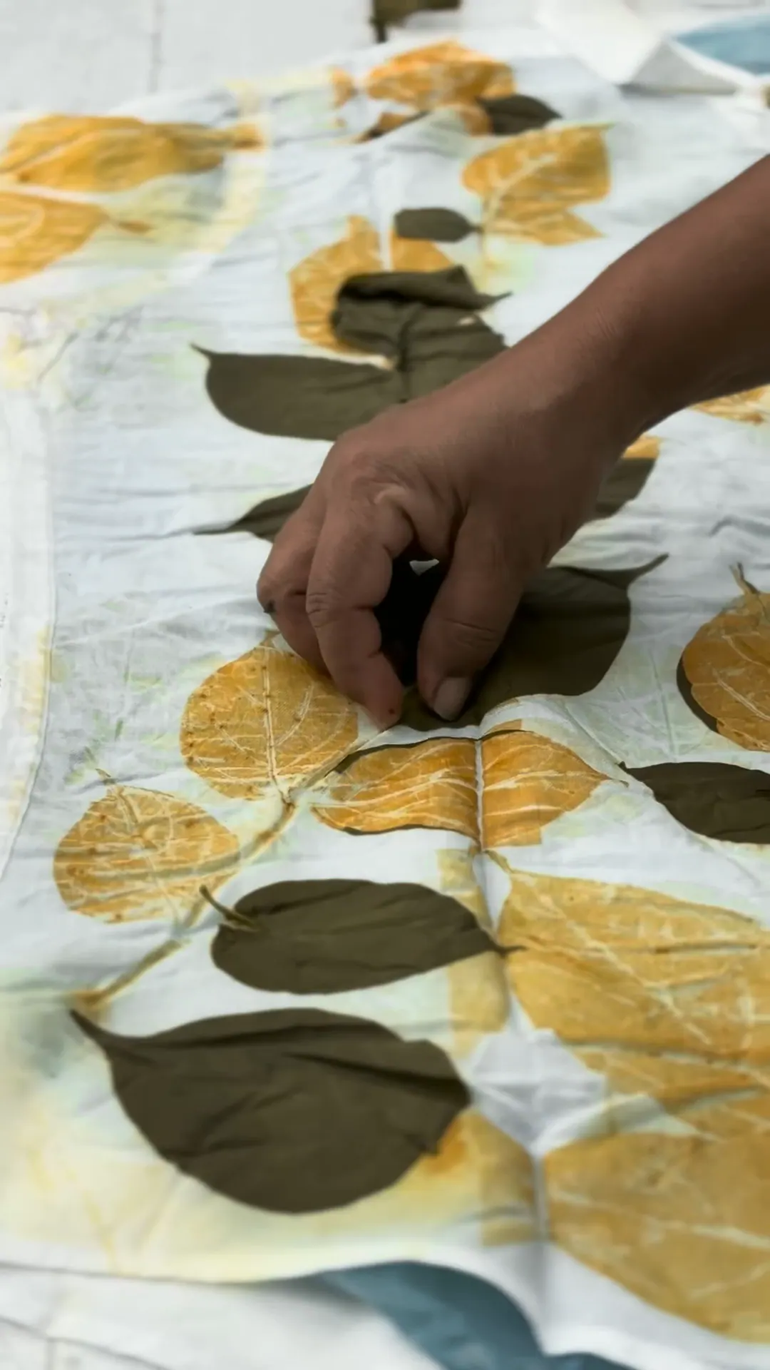 A hand lifts dark, steamed leaves away to reveal golden leaf prints beneath.