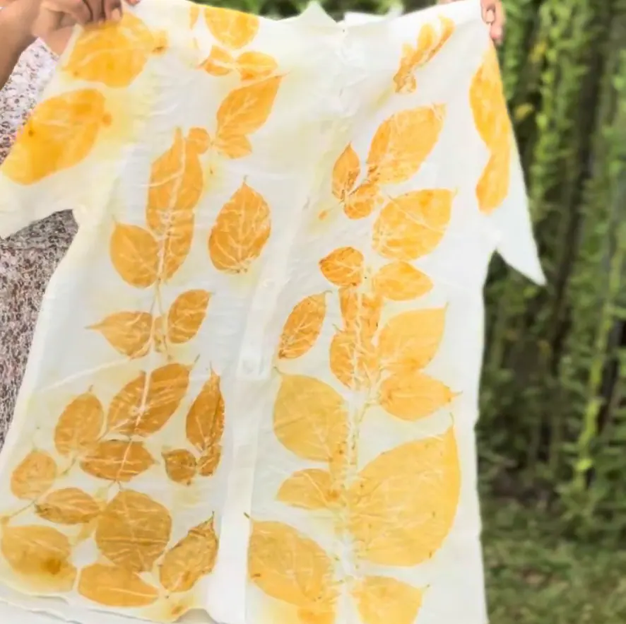 The golden-leaf shirt held up in the garden, its front and sleeves covered in leaf prints.