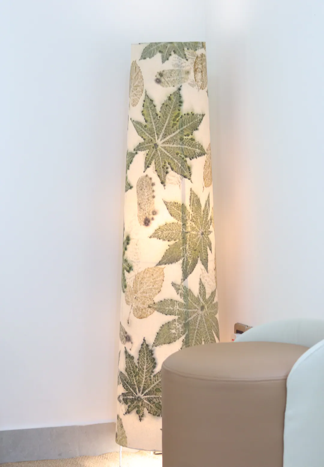 The eco-printed floor lamp, its shade printed with palmate leaves in sage and moss green, standing in a bright corner.
