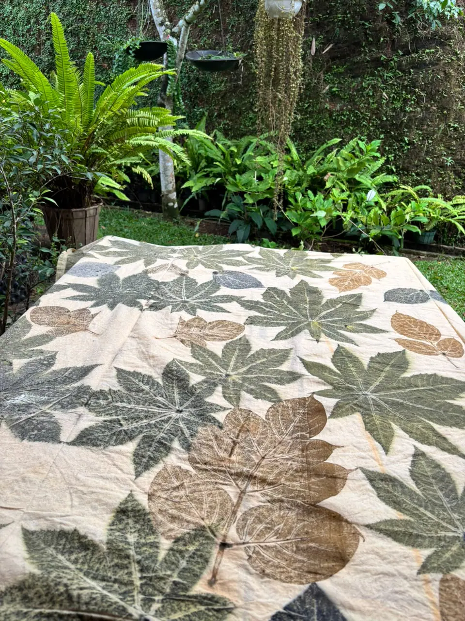 The palmate-leaf cloth seen at an angle on a garden table, its prints in sage, olive and umber.
