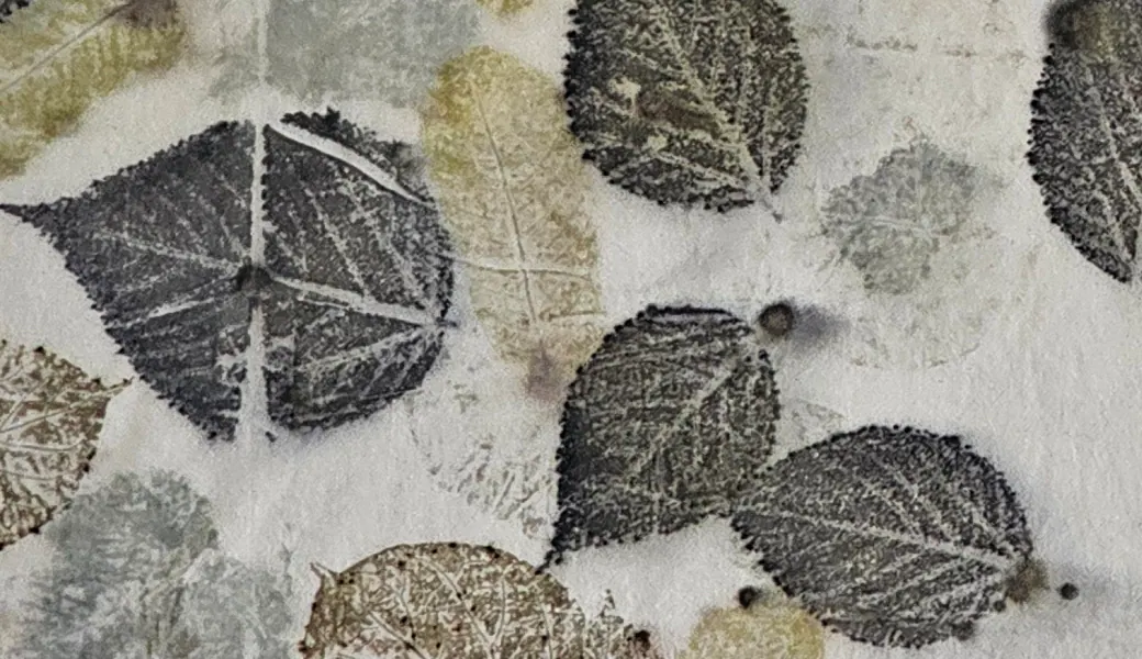 Close-up of charcoal leaf prints with crisp serrated edges on ivory cloth.