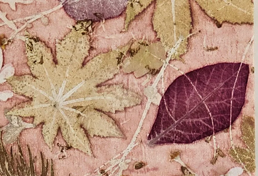 Close-up of a burgundy leaf print beside a pale palmate leaf on blush-pink cloth.